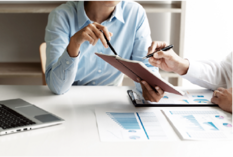 On voit une personne tenant un calepin à la main proposant quelque chose à une tierce personne. Ils sont autour d'un bureau evc un ordinateur, des feuilles de statistiques, stratégie marketing, devis.